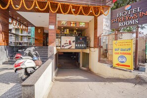 A hotel entrance with a sign for 'Hotel Shreyas Inn Rooms'. There is a scooter parked outside and a sign indicating car parking. - Fabhotel Shreyas Inn (Bengaluru)