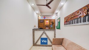A hotel reception area with a reception desk, a sofa, a ceiling fan, and a wall with a piano and decorative elements. - Fabhotel Shreyas Inn (Bengaluru)