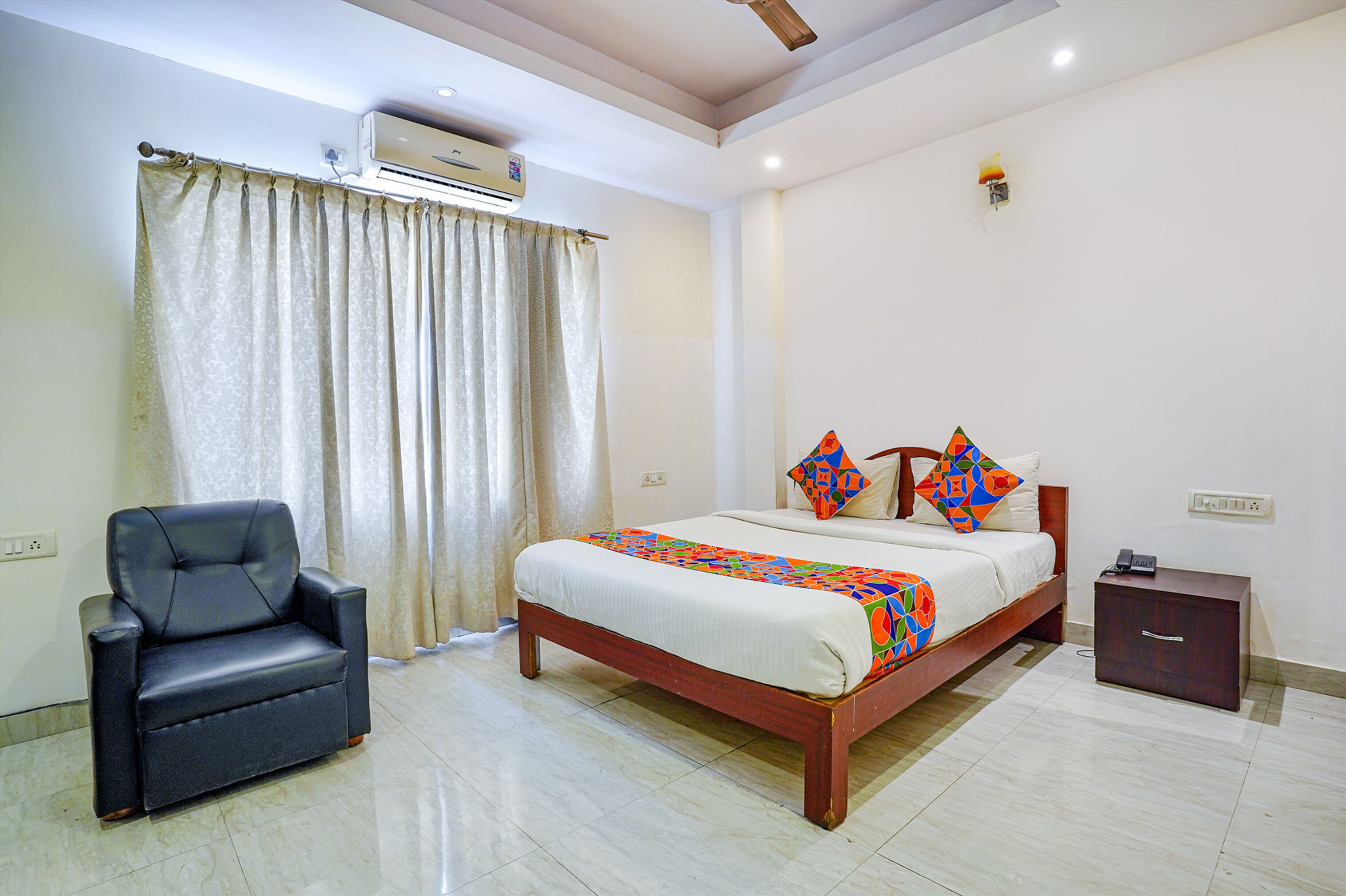 A bedroom with a bed, a chair, a bedside table, and an air conditioning unit.