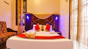 A hotel room with a large bed, a bedside table, a lamp, and a window with curtains. - Fabescape Queens Paradise (Vanur)