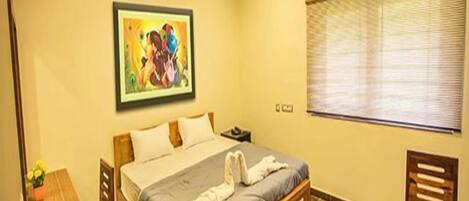 A bedroom with a bed, a desk, a chair, a ceiling fan, and a window with blinds.