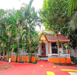 Un pequeño edificio de estilo tradicional con fachada roja y blanca, rodeado de abundante vegetación.