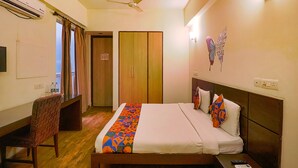 A hotel room with a bed, a chair, a desk, an air conditioner, a ceiling fan, and a wall decoration. - Fabhotel Merriment City (Noida)