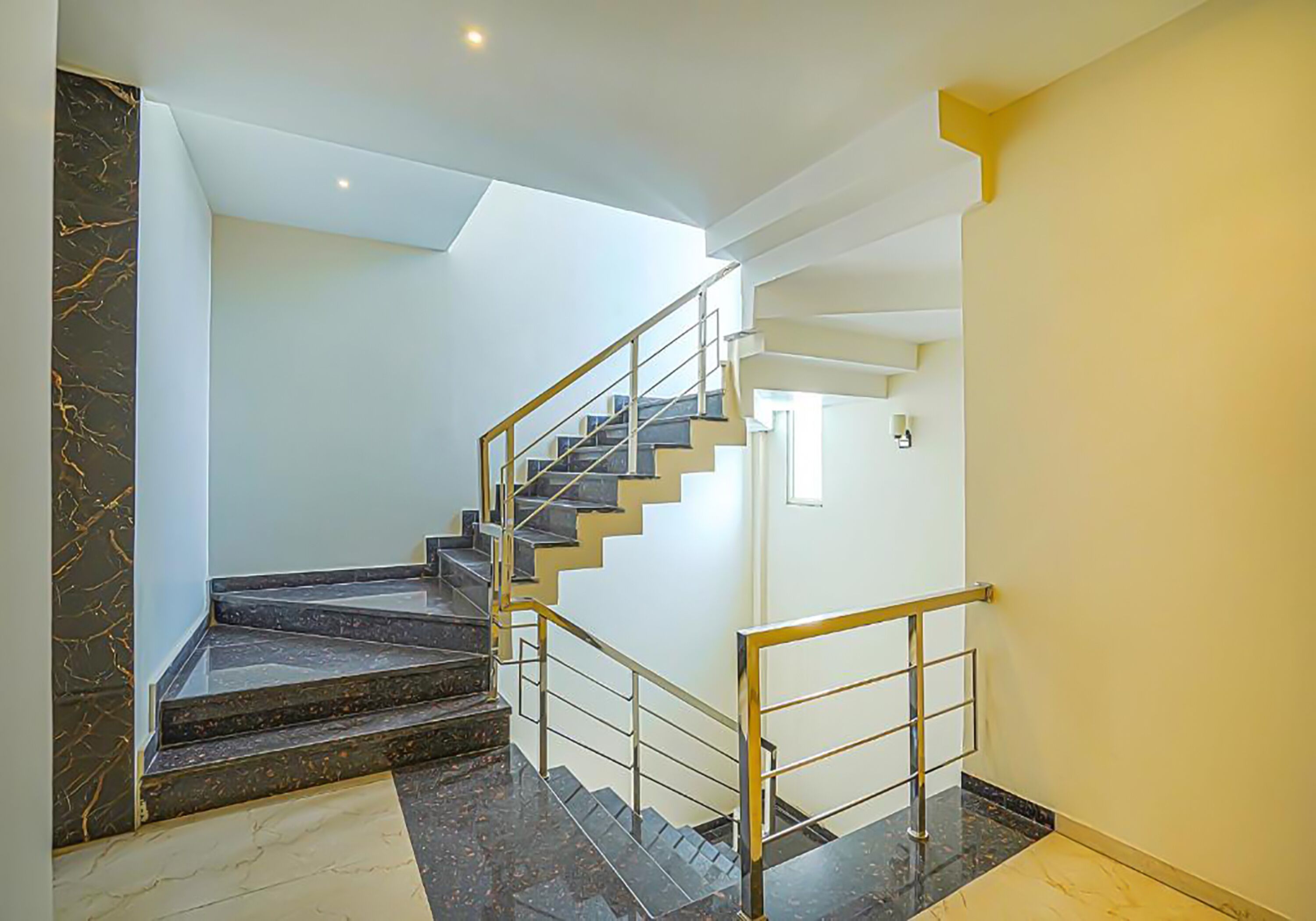 Una escalera moderna con barandilla de vidrio, escalones de mármol y una pared de color claro.