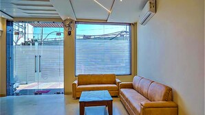 Un intérieur moderne avec un canapé et une table basse, de grandes fenêtres équipées de stores et un climatiseur fixé au mur.