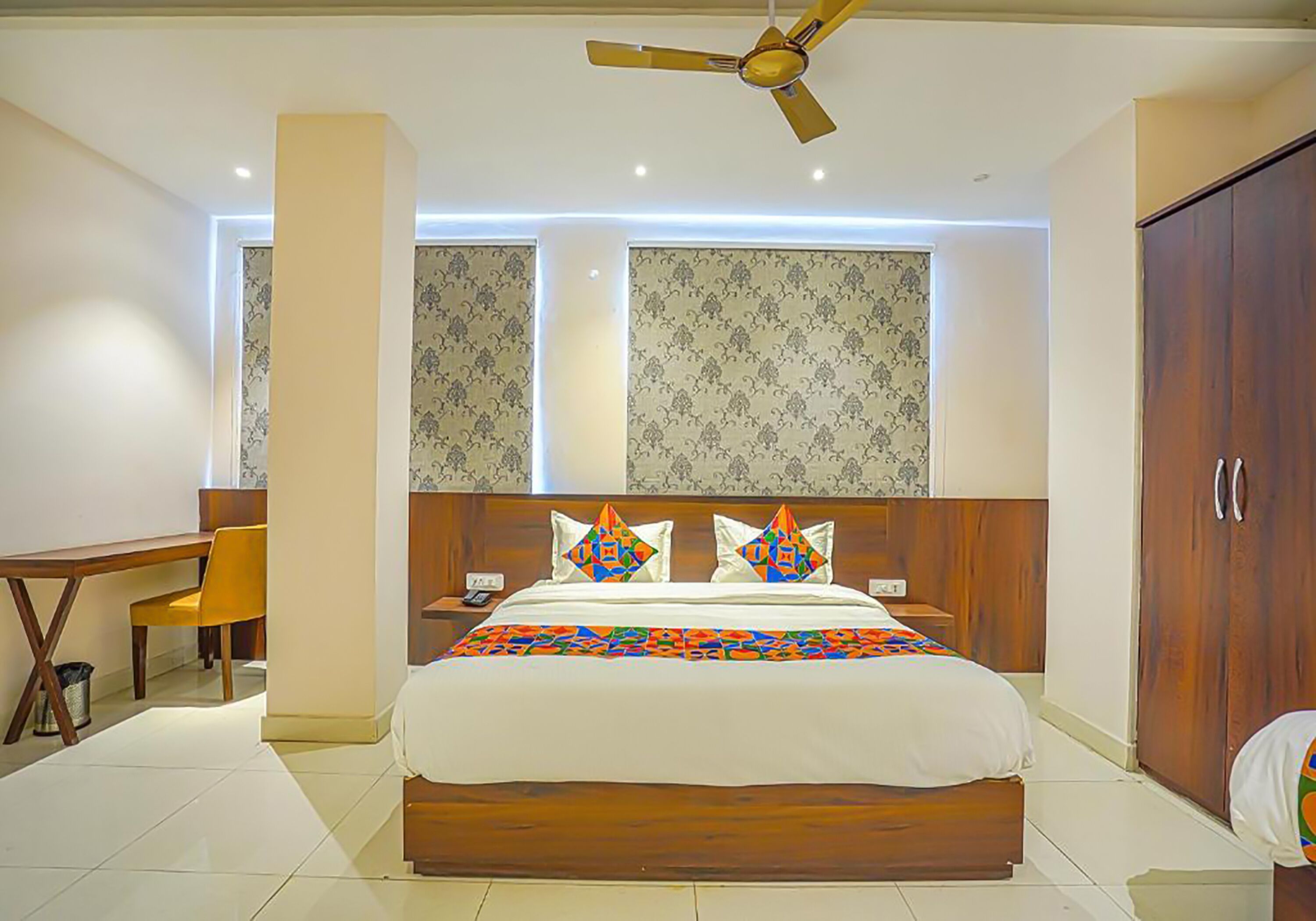A bedroom with a bed, a desk, a chair, a wardrobe, and a ceiling fan.
