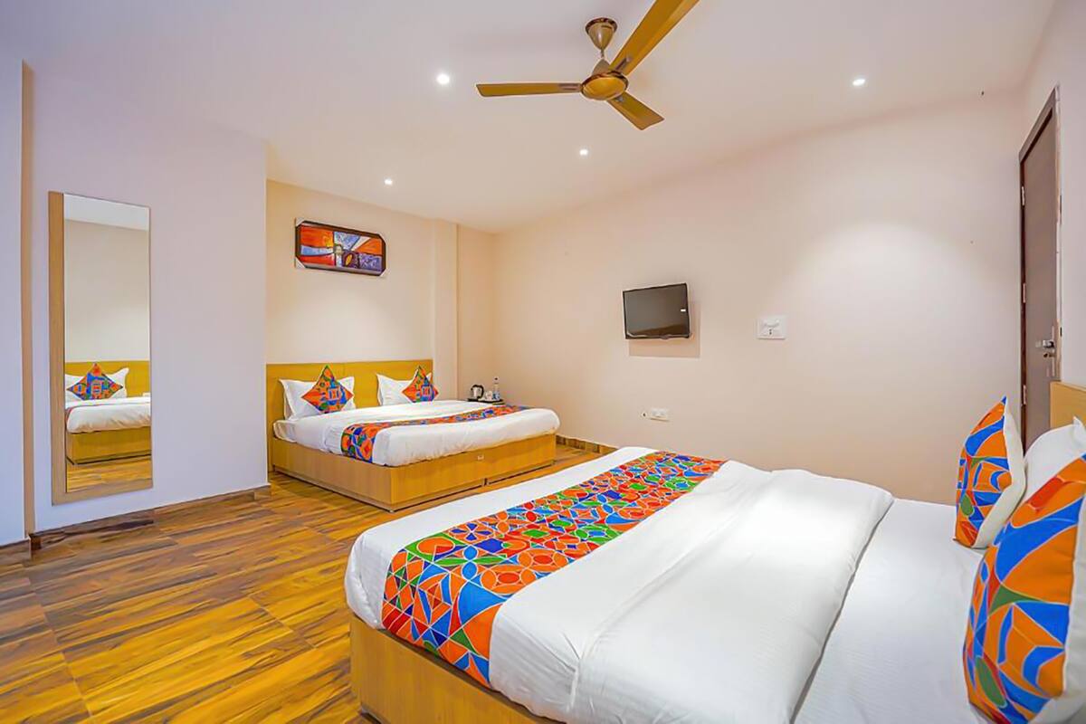 A hotel room with two beds, a ceiling fan, a TV, and a mirror.