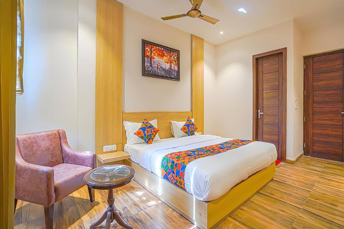 A hotel room with a bed, a chair, a small table, a ceiling fan, and a painting on the wall.
