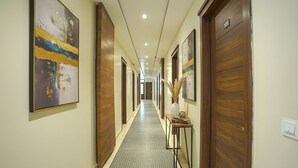 Un couloir d’hôtel avec des portes en bois, une moquette à motifs et des œuvres d’art accrochées aux murs.