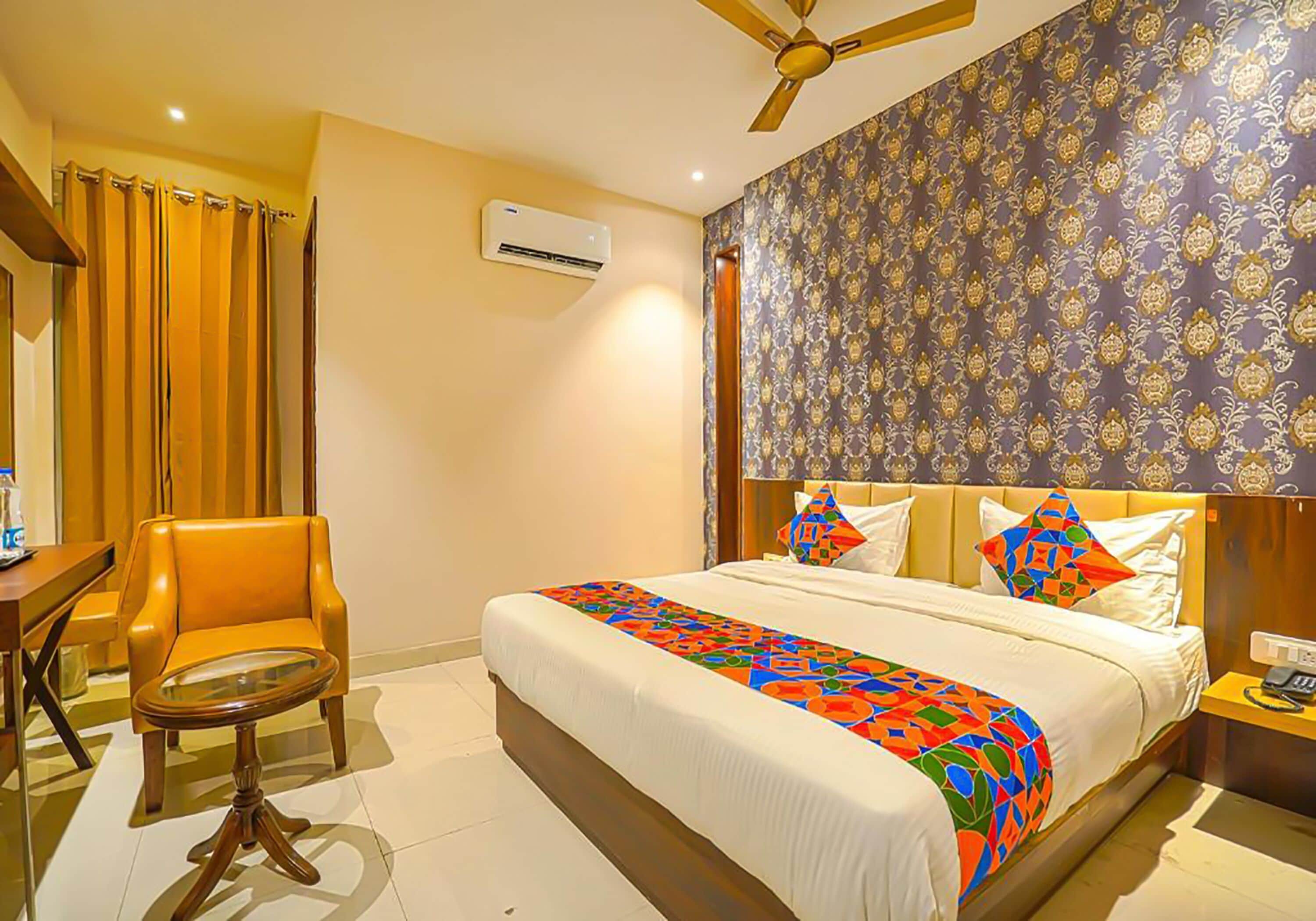A hotel room with a bed, a chair, a table, and a ceiling fan.