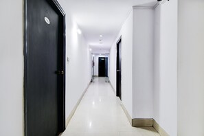 A long, narrow hallway with white walls and black doors, leading to a dark room at the end. - FabHotel Ballygunge Luxury - Behind Punjab Club (Kolkata)