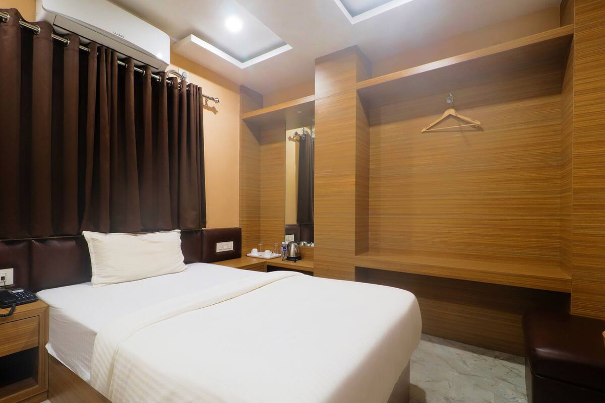 A hotel room with a large bed, a bedside table with a phone, a mirror, and a hanging coat rack.