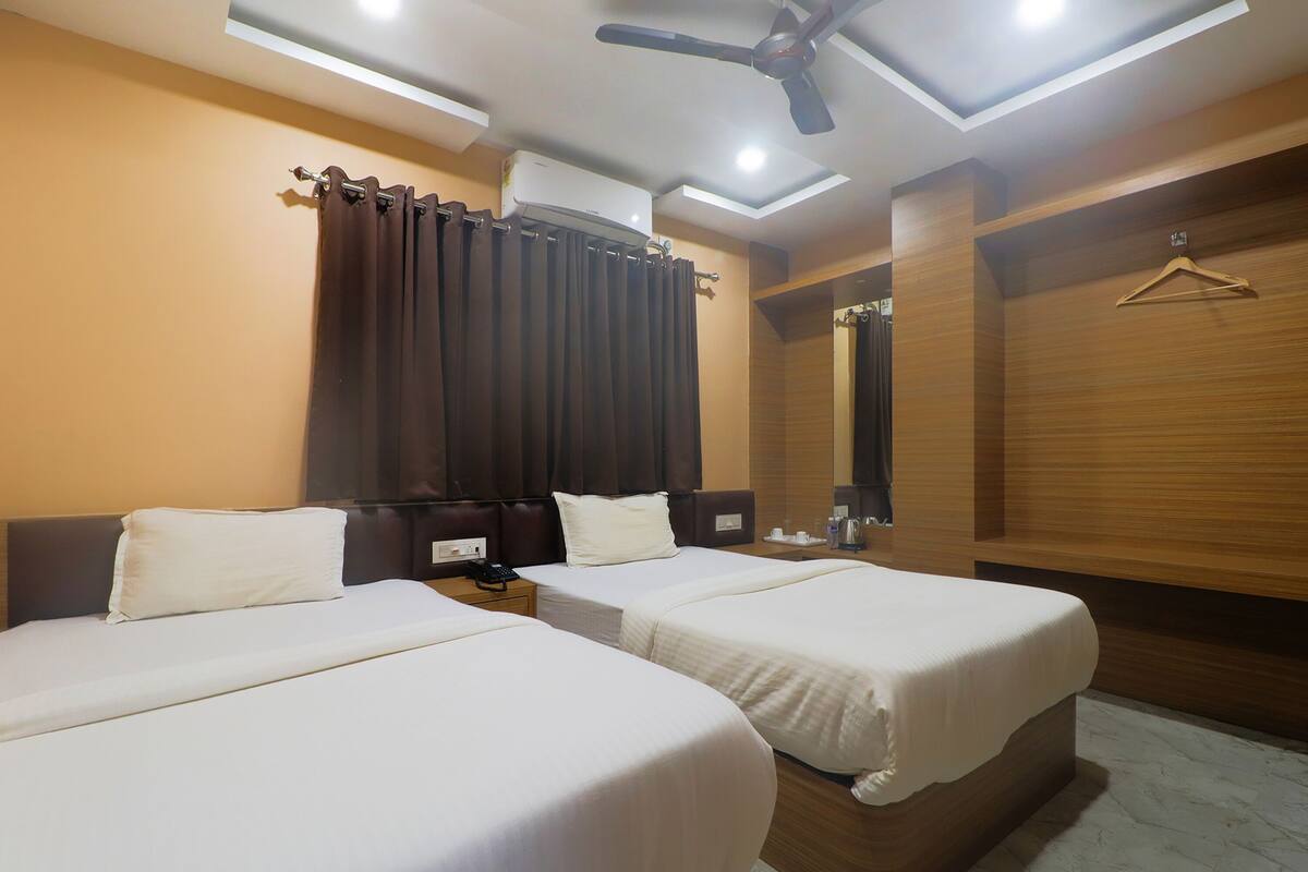 A hotel room with two beds, a ceiling fan, an air conditioning unit, a wooden wardrobe, and a hanging clothes rack.