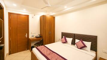 A hotel room with a bed, wooden wardrobe, desk, and a ceiling fan.