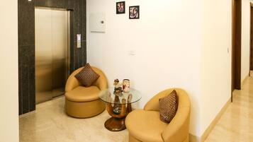 A modern living area with two beige armchairs, a glass coffee table, and a small statue.