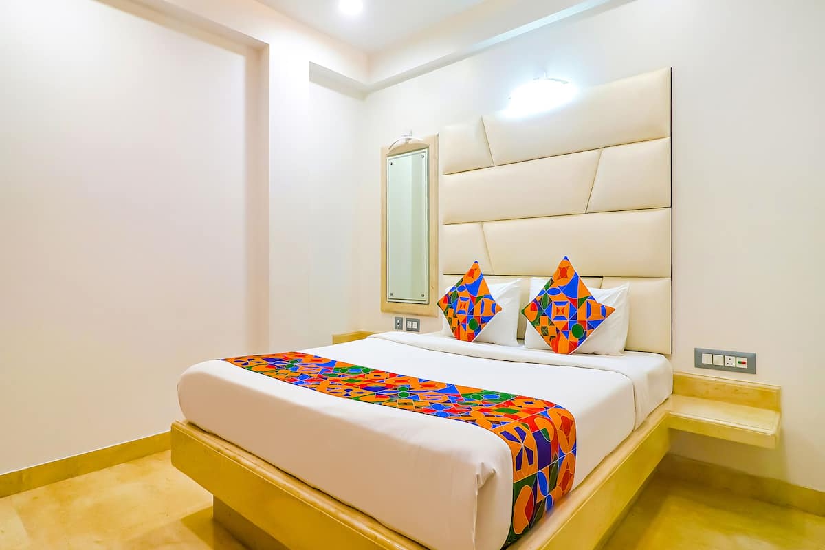 A hotel room with a bed, a bedside table, a nightstand, a mirror, and a wall-mounted light fixture.