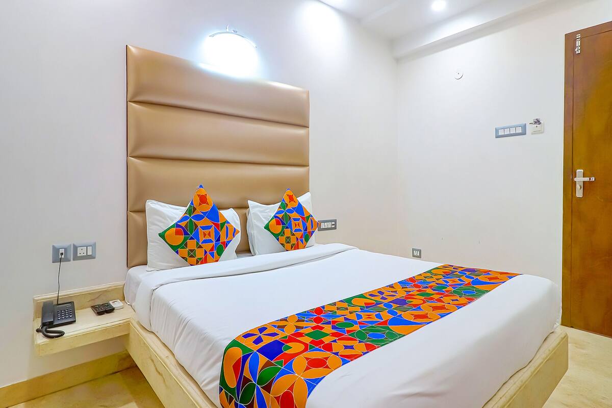 A hotel room with a large bed, a headboard, a bedside table with a phone, and a colorful throw blanket.