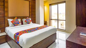 A modern hotel room with a large bed, a wooden headboard, a large window with a city view, and a desk with a remote control. - Fabhotel Eros 211 (Bidhannagar)