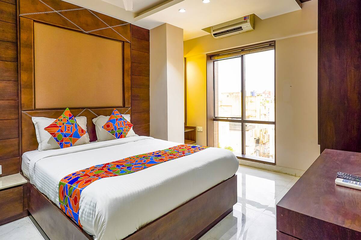 Una habitación de hotel moderna con una cama grande, cabecera de madera, un ventanal con vistas a la ciudad y un escritorio con un control remoto.