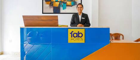 Un comptoir d’accueil aux couleurs bleu et orange, un logo représentant la chaîne « fab hotels », et une peinture abstraite moderne accrochée au mur.