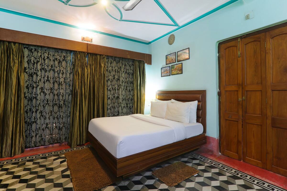 A bedroom with a large bed, a wooden wardrobe, and patterned curtains.