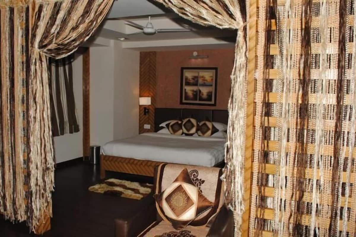 Una habitación con cama, cortinas, cabecero, una lámpara de pared y un cuadro enmarcado.