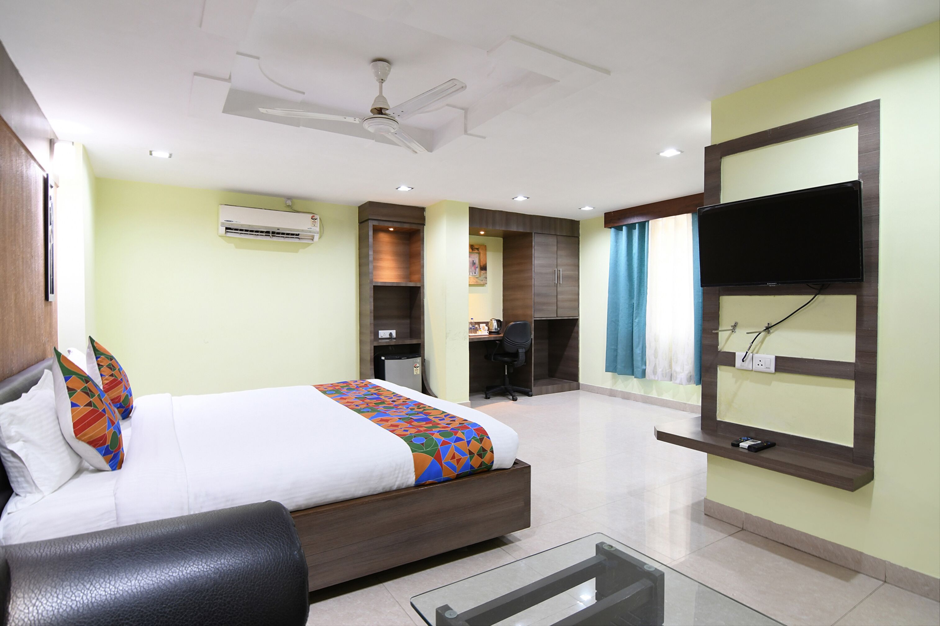 A hotel room with a bed, desk, chair, TV, air conditioning unit, and a ceiling fan.