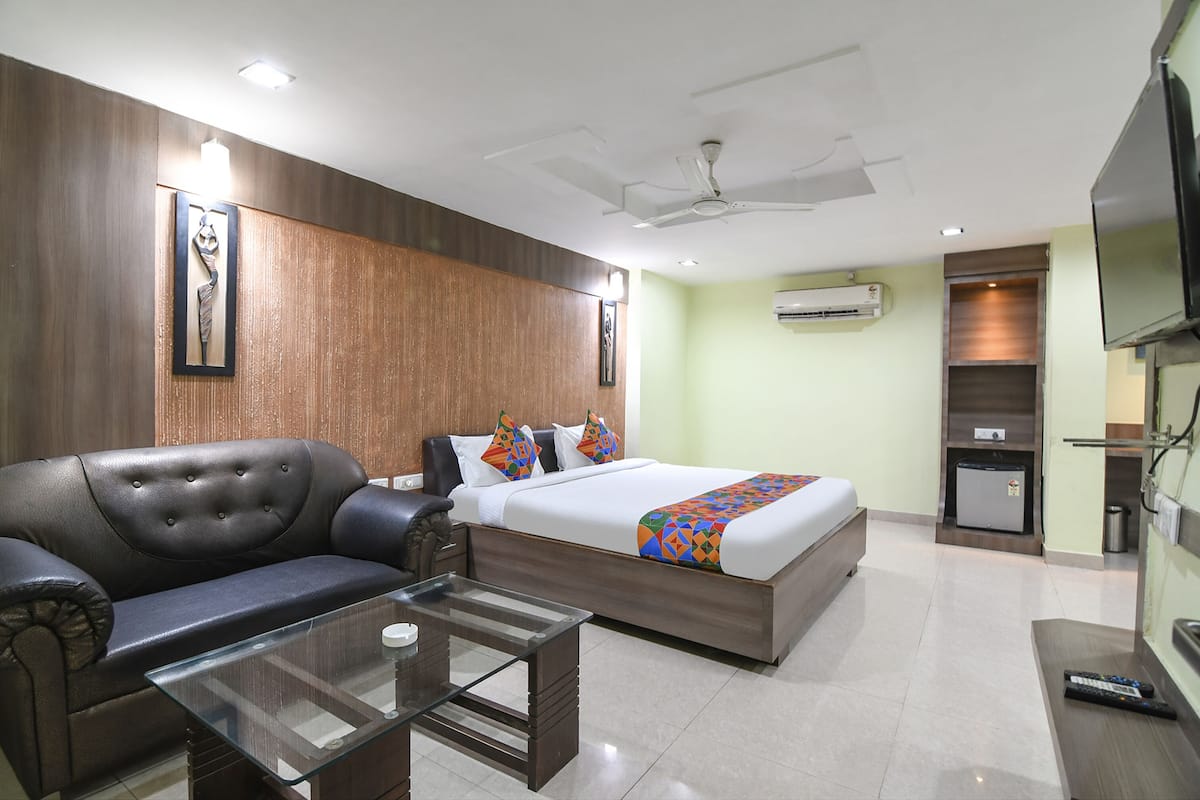 Una habitación de hotel con una cama, un sofá, una mesa de centro de vidrio, un ventilador de techo, un equipo de aire acondicionado y un televisor.