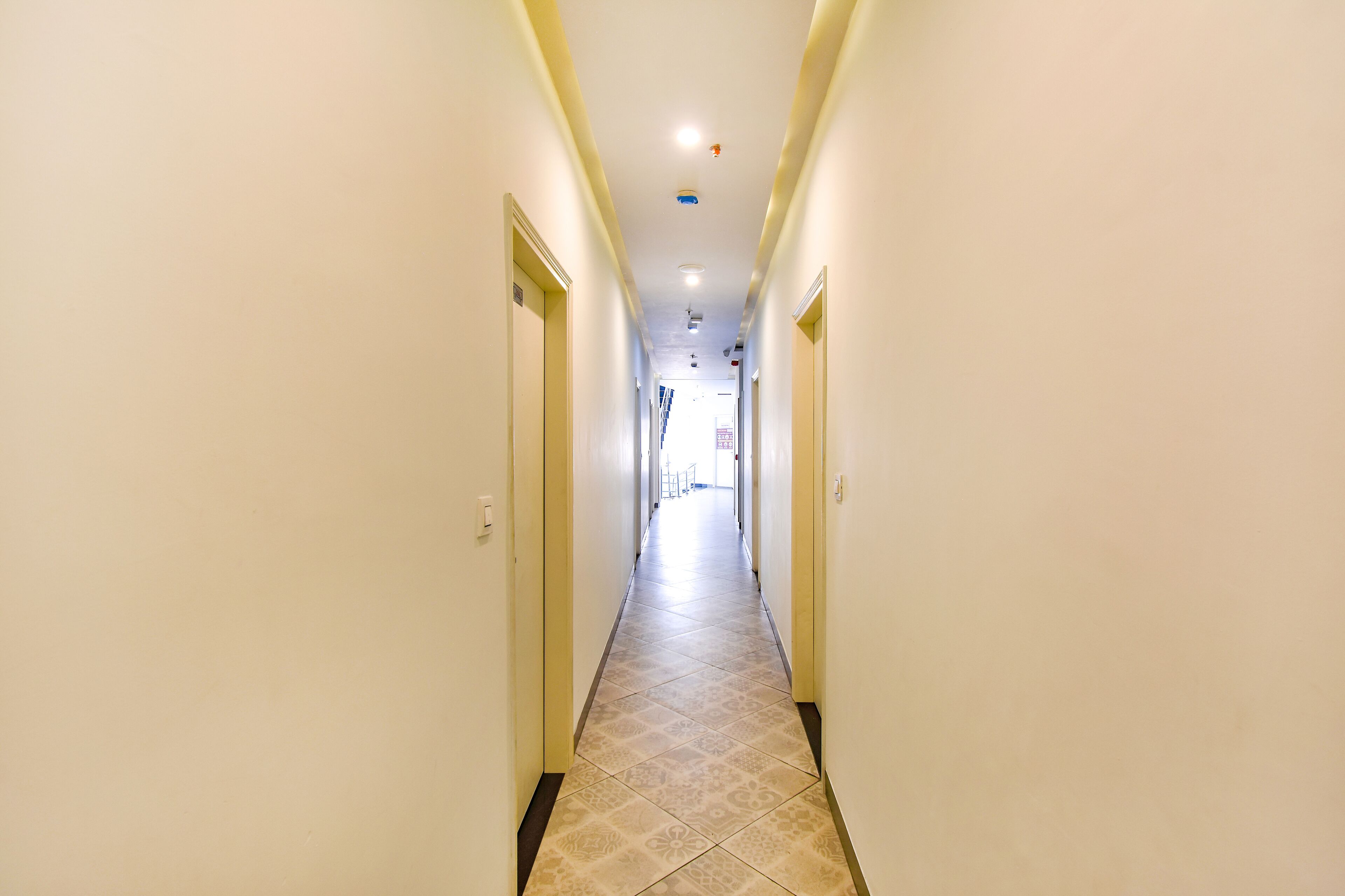 Un largo y estrecho pasillo de hotel con baldosas de diseño en el suelo, paredes blancas y puertas a ambos lados.