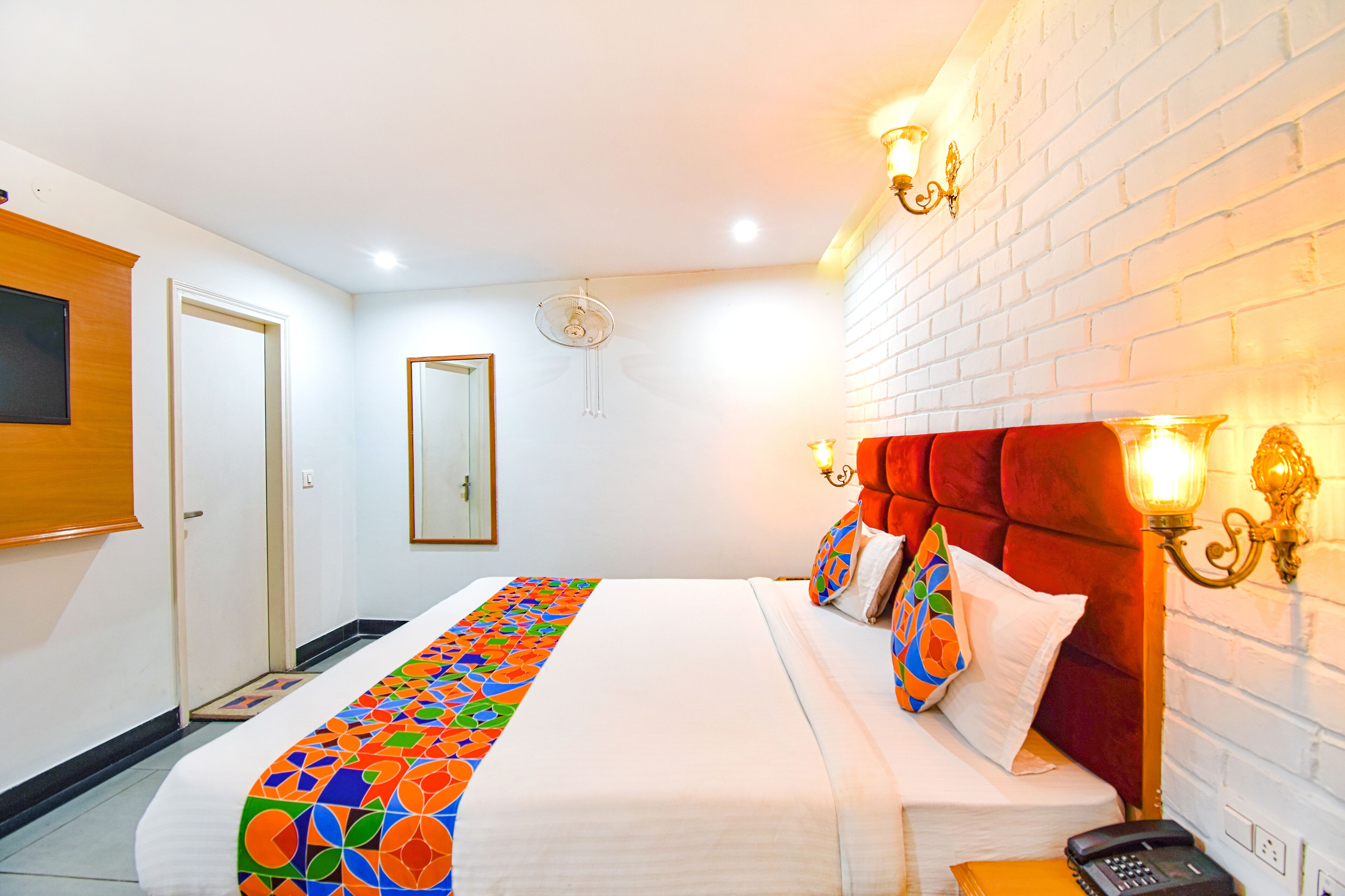 A hotel room with a bed, a bedside table, a telephone, and a wall-mounted light fixture.