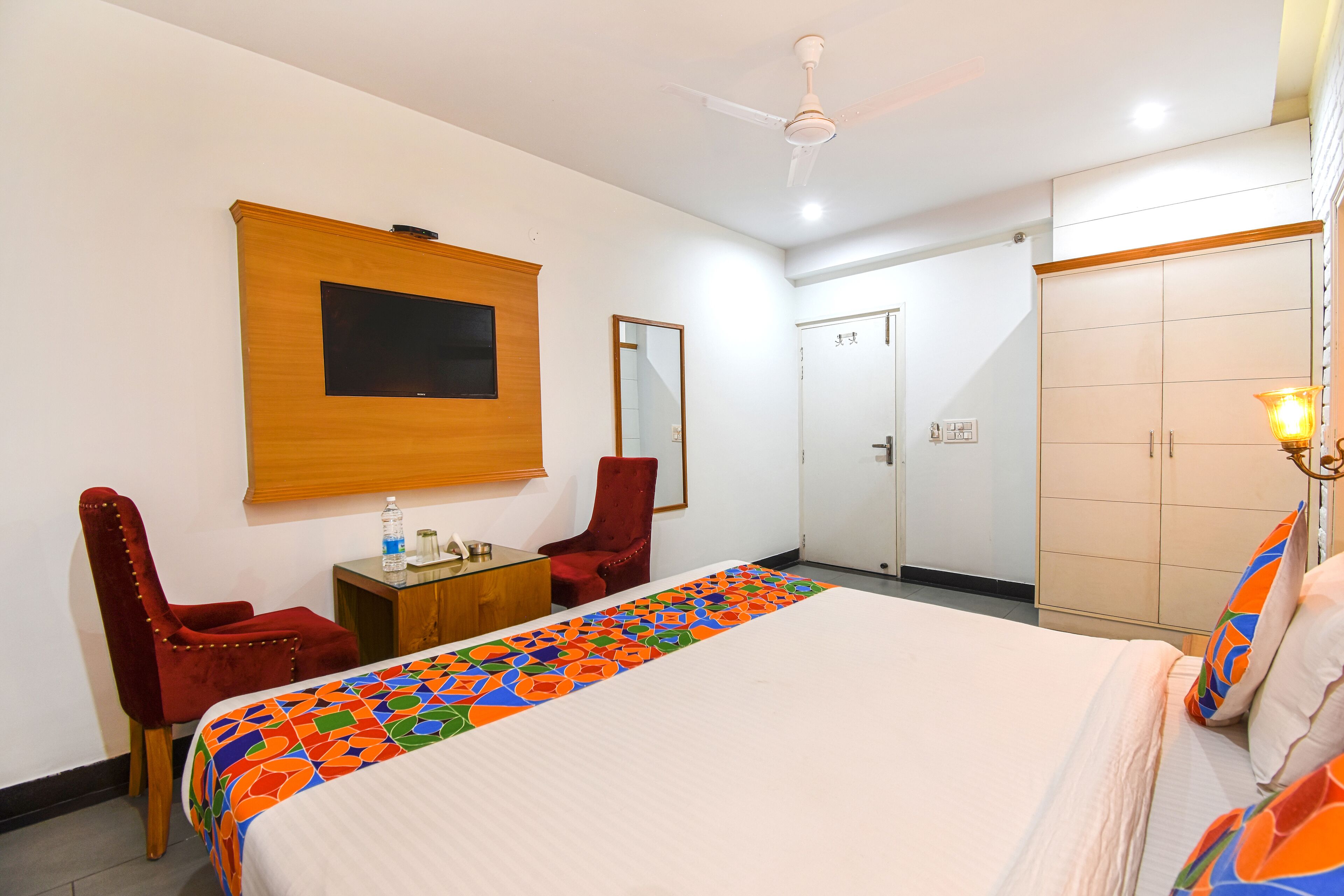 A hotel room with a bed, a desk, a chair, a wardrobe, and a ceiling fan.