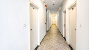Un long couloir étroit aux murs blancs et au sol recouvert de carreaux décoratifs, qui mène à plusieurs portes.
