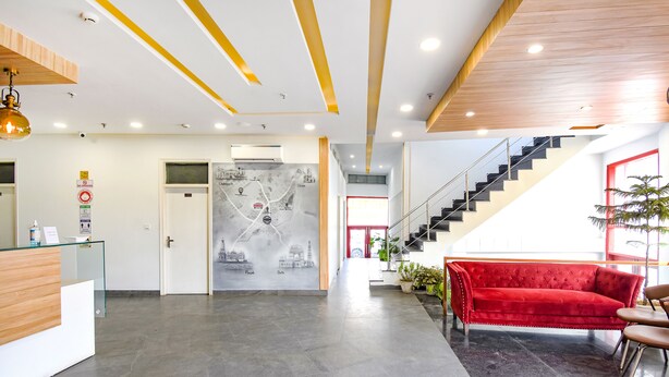 Un hall d’hôtel moderne avec un comptoir d’accueil, un canapé rouge, un escalier et une carte accrochée au mur.