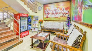 A hotel lobby with a Coca-Cola refrigerator, a staircase, a sofa, a coffee table, and a large painting of horses. - Fabexpress Ragu Residency (Coimbatore)