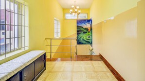 A hallway with yellow walls, a bench, a staircase, and a painting of a landscape. - Fabexpress Ragu Residency (Coimbatore)