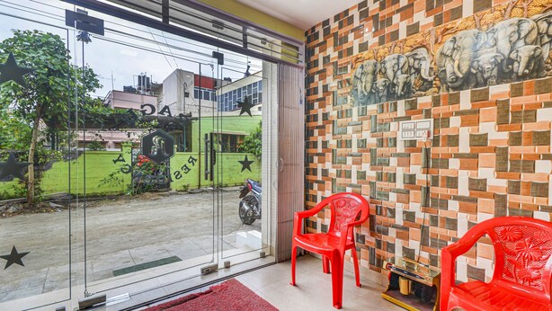 A room with a glass door leading outside, a tiled wall with an elephant mural, and two red plastic chairs. - Fabexpress Ragu Residency (Coimbatore)