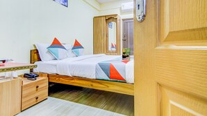 A bedroom with a wooden bed, a bedside table, a nightstand, and a mirror. - Fabexpress Ragu Residency (Coimbatore)