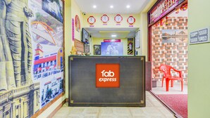 A reception area with a 'fab express' sign, a reception desk, a clock, and a red chair. - Fabexpress Ragu Residency (Coimbatore)