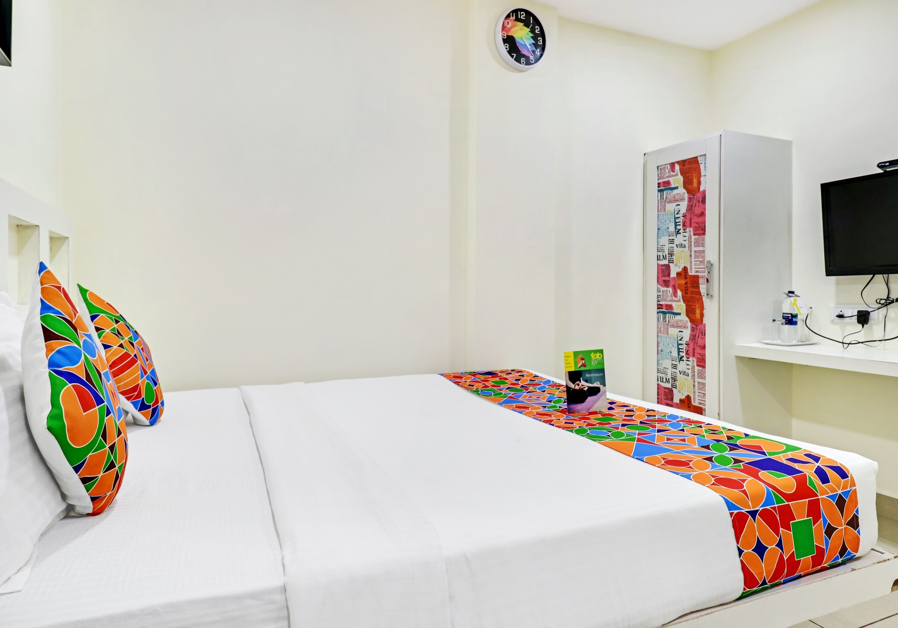 A hotel room with a bed, pillows, a TV, a desk, and a refrigerator.