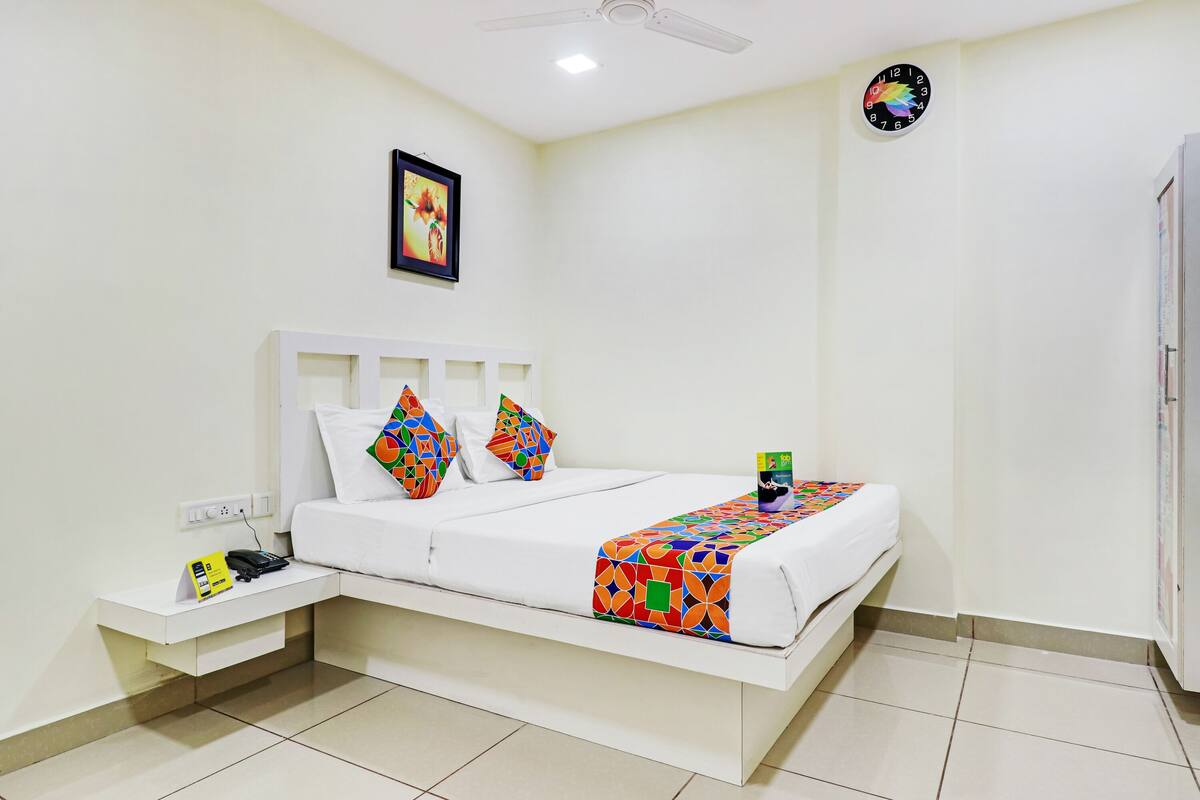 Une chambre à coucher bien rangée, avec un lit, des oreillers, une table de chevet, une horloge et un ventilateur de plafond.