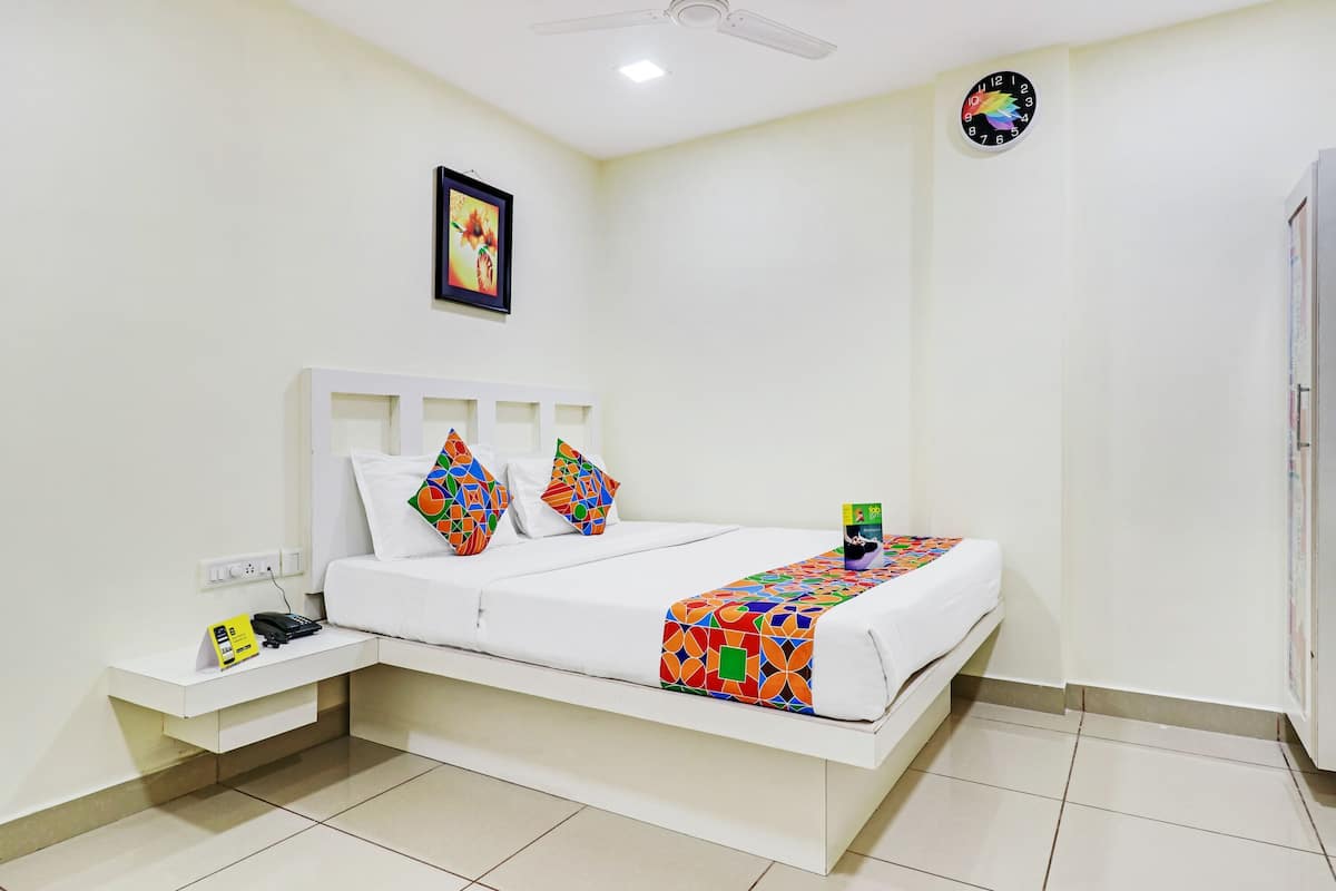 Une chambre à coucher bien rangée, avec un lit, des oreillers, une table de chevet, une horloge et un ventilateur de plafond.
