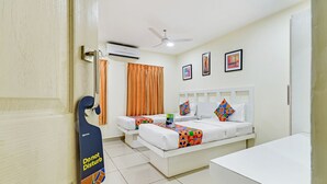 Una habitación de hotel con dos camas, un escritorio blanco, un ventilador de techo y un equipo de aire acondicionado.