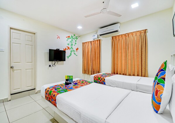 Una habitación de hotel con dos camas, televisión, equipo de aire acondicionado y cortinas estampadas.