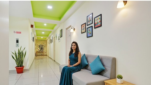 Un vestíbulo de hotel con techo verde, un sofá con cojines azules, una mesita de madera y cuadros enmarcados en la pared.