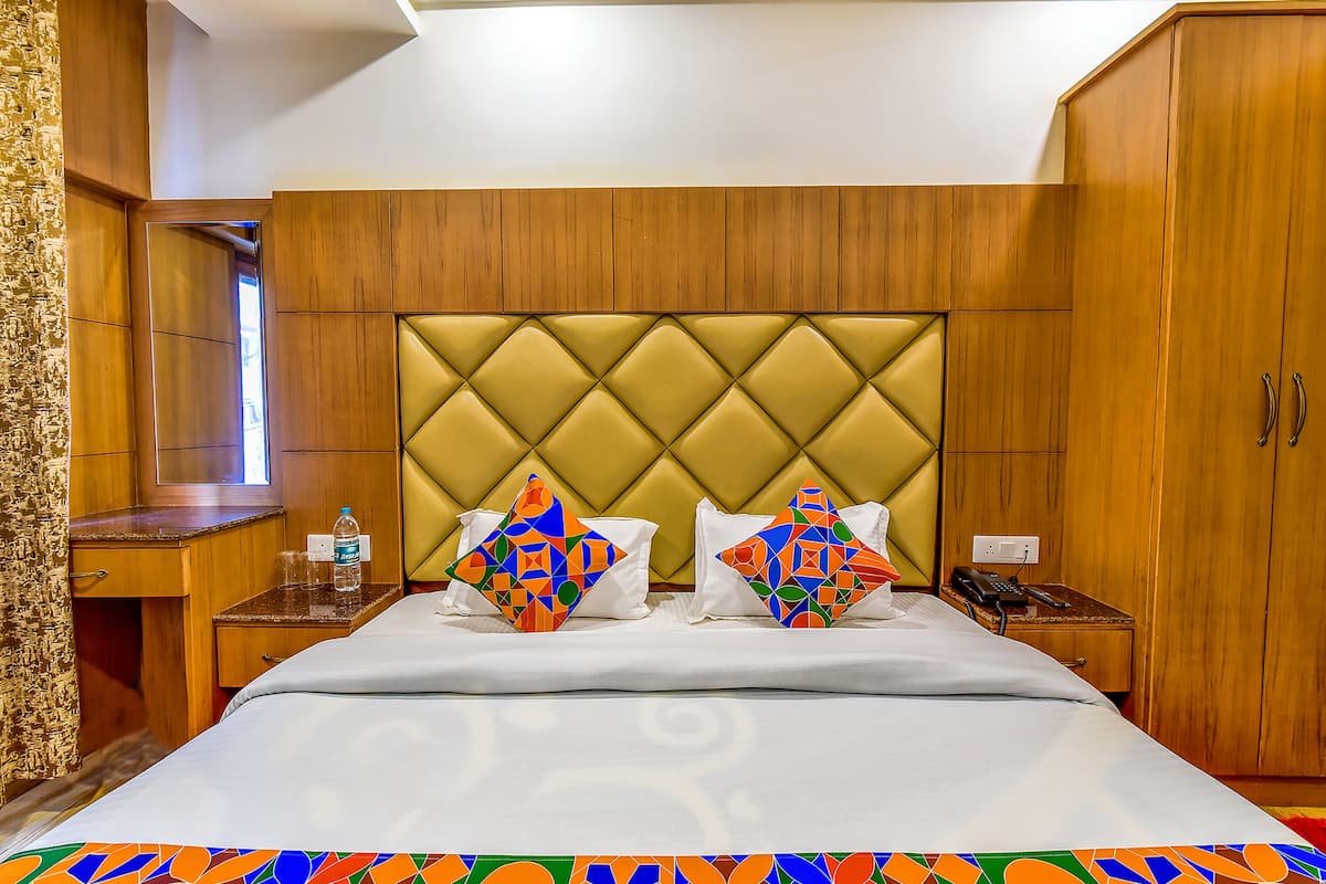 Una habitación de hotel con una cama grande, dos mesitas de noche, un armario de madera y un escritorio pequeño con un espejo.