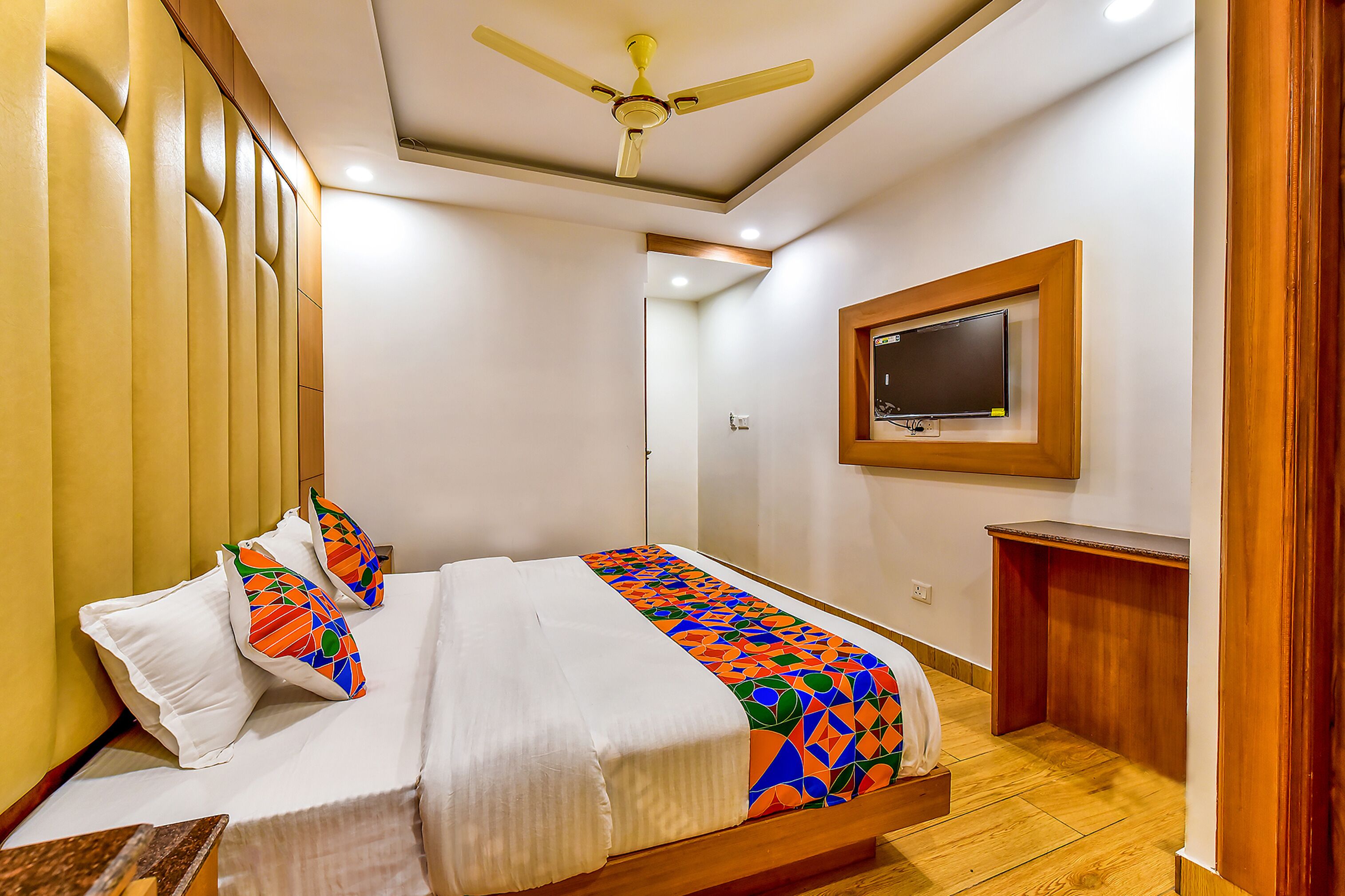 A neatly arranged bedroom with a bed, a television mounted on the wall, and a ceiling fan.
