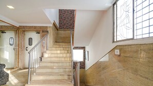 Una escalera con barandilla de metal, pared de ladrillo y ventana con diseño geométrico.