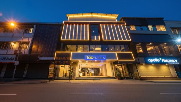 Un hotel moderno con un llamativo letrero de 'fab hotels', una farmacia al otro lado de la calle y una entrada bien iluminada.