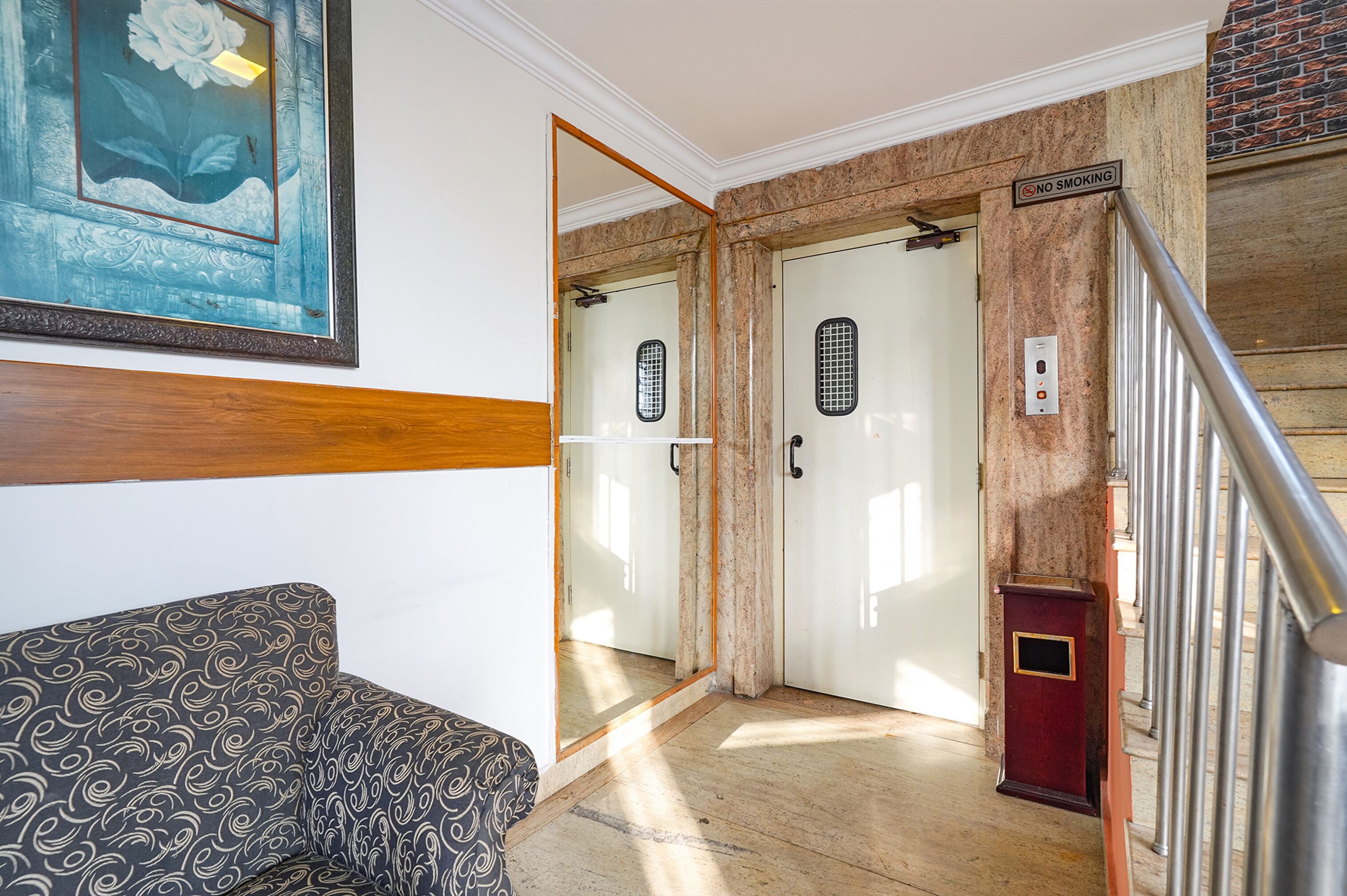 A hallway with a patterned sofa, a framed artwork, and a no smoking sign on a door.