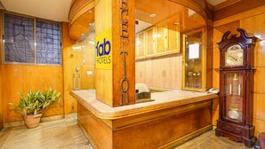 Una recepción con un cartel de 'Fab Hotels', una planta en maceta, un armario de madera y un reloj montado en la pared.